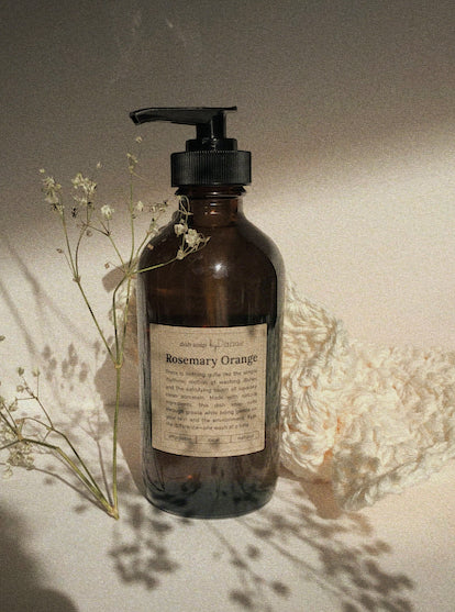 dark bottle of rosemary orange dish soap with little white flowers and a white cloth surrounding it.